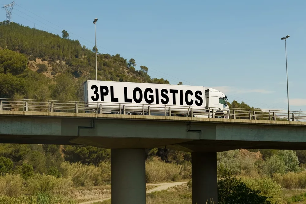 A white truck with "3PL LOGISTICS" in bold black letters drives across a bridge. The background features green hills and a clear blue sky.